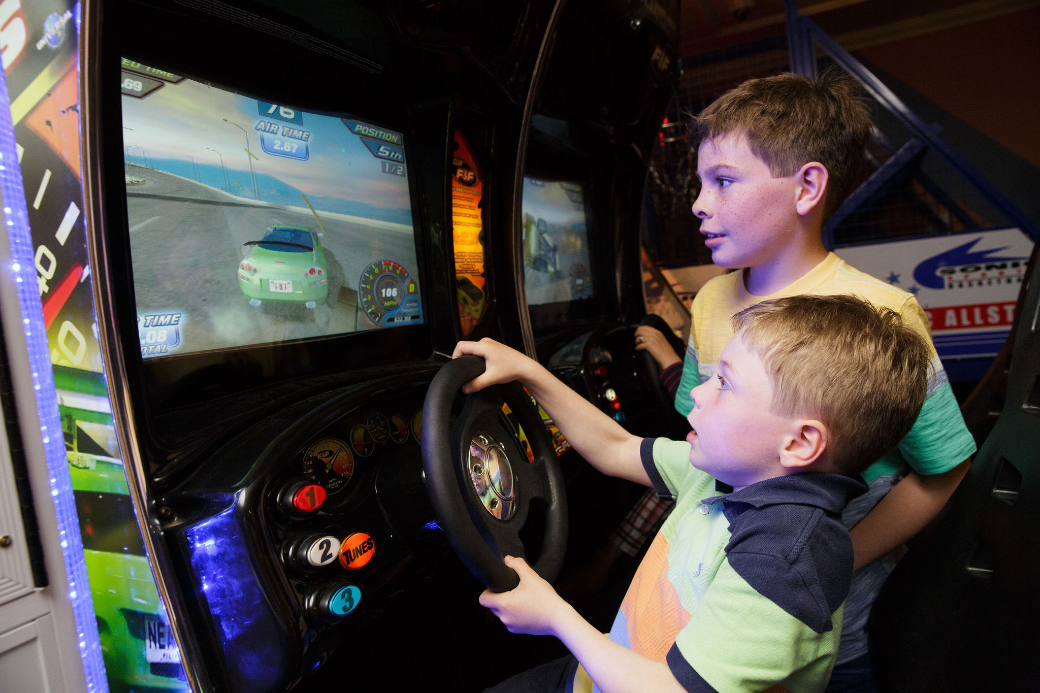 Two boys play a driving arcade game