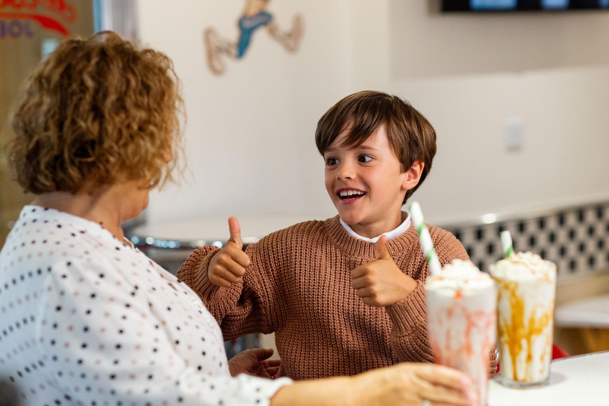 Young boy puts his thumbs up whilst enjoying a milkshake